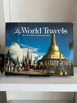 Book titled 'World Travels' with a blue cover featuring a stupa and people on a white shelf.