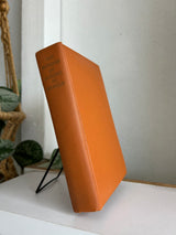 Orange book on a white surface with a plant in the background